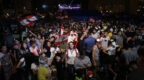 Young woman in crowd of people, at what looks like a political protest or gathering, Lebanese flags being waved.