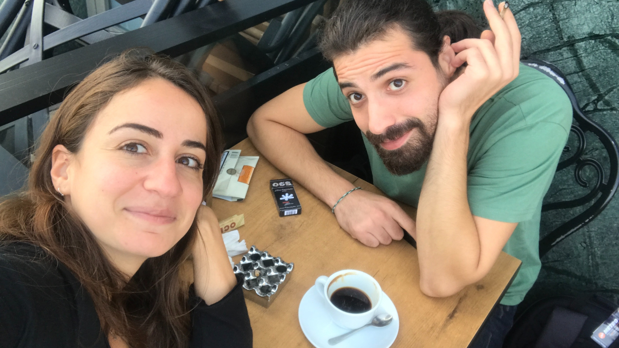 Janay and Habak with coffee and cigarettes, smiling at the camera